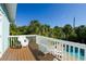 Relax on the wooden balcony with white wicker furniture overlooking lush greenery and the pool below at 507 Spring Ave, Anna Maria, FL 34216