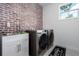 This laundry room features brick accent wall, modern washer and dryer, plus sink with white cabinets at 5651 Trevesta Pl, Palmetto, FL 34221