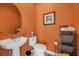 Small powder room has an orange wall color, a round mirror, a pedestal sink and a standard toilet at 6907 47Th E Ct, Ellenton, FL 34222