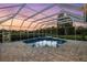 Screened-in backyard pool with stone pavers surrounded by lush greenery at dusk with purple sky at 7832 Panther Ridge Trl, Bradenton, FL 34202