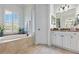 This primary bathroom features a tiled, columned tub, tile flooring, vanity with mirror, and a window with shutters at 2152 Majestic Oaks Blvd, Clearwater, FL 33759
