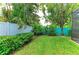 Backyard with green lawn, white fence, and turquoise accent wall with tropical landscaping at 5386 Creekside Trl, Sarasota, FL 34243
