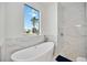 Bright bathroom showcasing a modern soaking tub, marble accents, a rainfall shower, and a window with neighborhood views at 6146 Grandeur St, Englewood, FL 34224