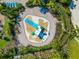 Aerial view of a splash pad with slides and a surrounding brick patio, lined with lounge chairs and lush landscaping at 12712 Dusty Trail Dr, Sarasota, FL 34238