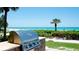 Outdoor BBQ area with a modern stainless steel grill, stone countertop, tropical plants, and a beautiful beach view at 1945 Gulf Of Mexico Dr # M2-313, Longboat Key, FL 34228