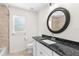 Bright bathroom with black granite countertop, white cabinets, and round mirror at 2575 Johannesberg Rd, North Port, FL 34288