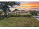 Charming one-story home featuring a covered porch, well-manicured lawn, and vibrant sunset backdrop at 1651 Red Oak Ln, Port Charlotte, FL 33948