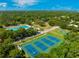 Lovely aerial view of a tennis courts and pool surrounded by green trees and blue skies at 2110 Craft Ln, Sarasota, FL 34239