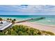 Picturesque view of a pier extending into the turquoise sea, complemented by nearby palm trees and beachfront buildings at 321 Sorrento Dr, Osprey, FL 34229