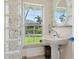 Bathroom with a pedestal sink, round mirror, and a glass block window allowing natural light at 7779 Holiday N Dr, Sarasota, FL 34231