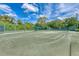 Outdoor tennis court with green surface, surrounded by lush trees, under a partly cloudy, blue sky at 8525 54Th Avenue E Cir, Bradenton, FL 34211