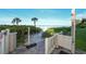 A sandy path leads to the beach, accompanied by a shower and foot washing station, tropical foliage, and clear skies at 19 Whispering Sands Dr # 805, Sarasota, FL 34242