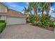 Two-car garage on a home with a red tile roof, brick driveway, and tropical landscaping at 23233 Banbury Way # 302, Venice, FL 34293