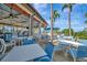Outdoor patio seating under a covered area, with white tables and blue chairs near palm trees at 23233 Banbury Way # 302, Venice, FL 34293