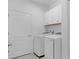 Well-lit laundry room with a white washer, dryer, storage cabinets, and door at 2578 Wild Cherry Path, Sarasota, FL 34240