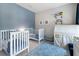 Charming bedroom with two white cribs, blue accent wall and blue rug for a peaceful and stylish space at 5718 Title Row Dr, Bradenton, FL 34210