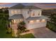 A stunning two-story home features a three-car garage, lush landscaping, and elegant curb appeal at twilight at 5718 Title Row Dr, Bradenton, FL 34210
