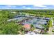 Aerial view of tennis courts with covered seating areas, surrounded by lush landscaping and a lake at 7716 Uliva Way, Sarasota, FL 34238