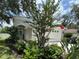 Charming home featuring a two-car garage, arched entrance, and lush landscaping with mature trees and flowering plants at 15207 Searobbin Dr, Lakewood Ranch, FL 34202