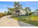 Charming stilt home with beautiful landscaping and a long driveway, surrounded by mature palm trees under a blue sky at 221 85Th St, Holmes Beach, FL 34217