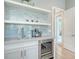 Wet bar features custom white cabinets, wine fridge, open shelving, and a decorative backsplash with a sink at 7838 Bowspirit Way, Lakewood Ranch, FL 34202