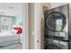 Neat laundry setup with stacked washer and dryer, next to a bedroom with vibrant red pillows and inviting light at 2201 Avenue C, Bradenton Beach, FL 34217
