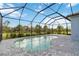View of the screened-in pool and brick paver deck against a scenic green backyard at 2794 Butterfly Jasmine Trl, Sarasota, FL 34240
