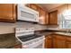 Kitchen boasting wooden cabinets, black countertops, and white appliances including a microwave and electric stove at 8730 Filson Pl, Sarasota, FL 34231
