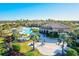 Stunning aerial view of the community pool and clubhouse with lush landscaping and palm trees under a clear blue sky at 12230 Amica Loop, Venice, FL 34293