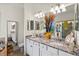 Bathroom features granite countertops, double sinks, white cabinetry, decorative vases and a clear glass shower at 12230 Amica Loop, Venice, FL 34293