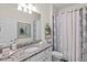 Well lit bathroom with granite countertops, white cabinetry, decorative mirror, and shower with patterned curtain at 12230 Amica Loop, Venice, FL 34293