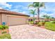 Paver driveway leading to a tan garage with palm trees at 12230 Amica Loop, Venice, FL 34293