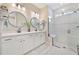 Bright bathroom featuring a double vanity, round mirrors, and a glass-enclosed shower with a bench seat at 42250 Ramble Rd, Punta Gorda, FL 33982