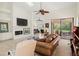Bright living room with a ceiling fan, fireplace, large brown leather sofa, and a view of the backyard at 7331 Villa D Este Dr, Sarasota, FL 34238