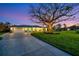 Beautiful dusk view of the light blue home with landscaped lawn, curved driveway and welcoming, illuminated front porch at 7817 Alhambra Dr, Bradenton, FL 34209