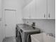 Bright laundry room featuring a washer, dryer, utility sink, tile flooring, and ample overhead cabinet storage at 8979 Grey Oaks Ave, Sarasota, FL 34238