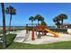 Fun playground with a slide, climbing net, and swings amidst swaying palm trees and ocean backdrop at 2055 Gulf Of Mexico Dr # G2-108, Longboat Key, FL 34228