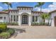 Charming home featuring a dark wood arched front door, white columns, lush landscaping, and a paver driveway at 8312 Catamaran Cir, Lakewood Ranch, FL 34202