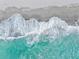 Aerial view of waves crashing on the shoreline, blending turquoise waters with sandy beach at 138 Tiziano Way, North Venice, FL 34275