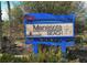 Manasota Beach sign in blue, with tan lettering featuring a serene beach theme, stands among coastal vegetation at 387 Eden Dr Dr, Englewood, FL 34223