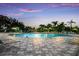 Large community swimming pool with sun loungers under a colorful sunset sky, surrounded by palm trees at 8640 Stone Harbour Loop, Bradenton, FL 34212