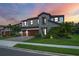 Beautiful two-story home featuring a stone facade, a three-car garage, and tropical landscaping against a vibrant sunset at 8932 Isabella Cir, Parrish, FL 34219