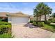 Beautiful home with a tile roof, white garage door, brick driveway, and lush landscaping including palm trees at 5866 Guarino Dr, Sarasota, FL 34238
