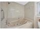 A close-up of a marble-look whirlpool bathtub with a showerhead, grab bar, and a small window at 7913 19Th Avenue W Dr, Bradenton, FL 34209