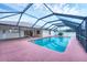 A covered, screened-in outdoor pool with tropical plants and a pink concrete pad surrounded by a white house with sliding glass doors at 408 Fletcher St, Port Charlotte, FL 33954