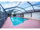 A covered, screened-in outdoor pool with tropical plants and a pink concrete pad surrounded by a white house at 408 Fletcher St, Port Charlotte, FL 33954