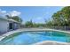 Backyard pool with wooden patio, white table and chairs surrounded by green trees on a sunny day at 4771 Riverwood Cir, Sarasota, FL 34231