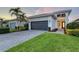 Inviting home featuring a paver driveway, dark garage door, manicured lawn, and tropical landscaping with palm trees at 5187 Barnett Cir, Lakewood Ranch, FL 34211