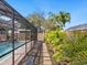 View of side yard featuring tropical landscaping, stepping stone pathway, and screened-in pool area at 7460 Dickens Dr, Sarasota, FL 34231