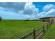 Expansive green lawn with a wooden fence, bordered by trees and buildings under a bright, partly cloudy sky at 8437 Nandina Dr, Sarasota, FL 34240